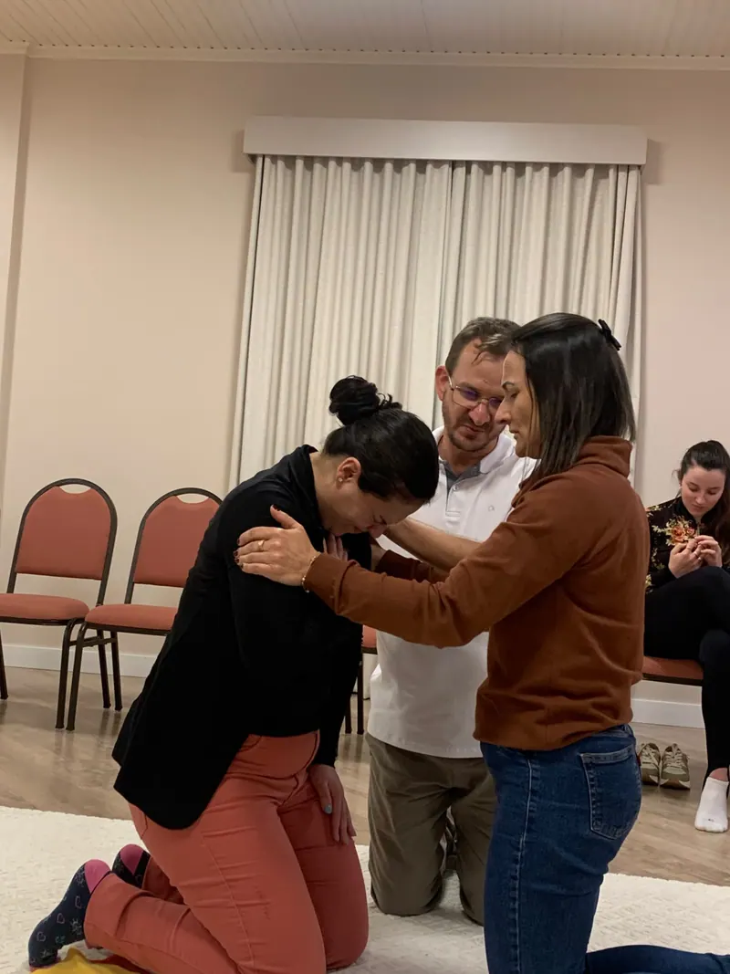 Participante de joelhos, acolhida por duas pessoas durante uma constelação
