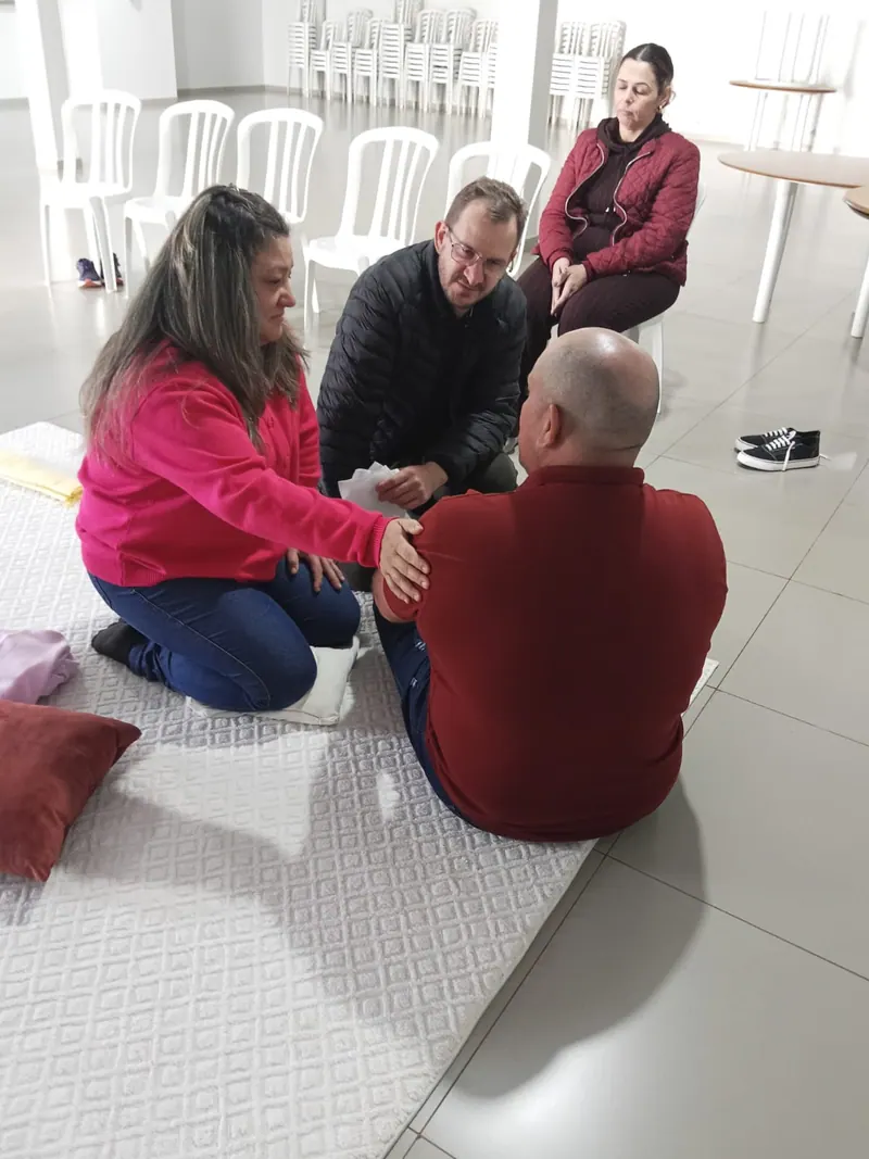 Edilson ao lado de uma participante que toca o ombro de outra durante o atendimento em grupo