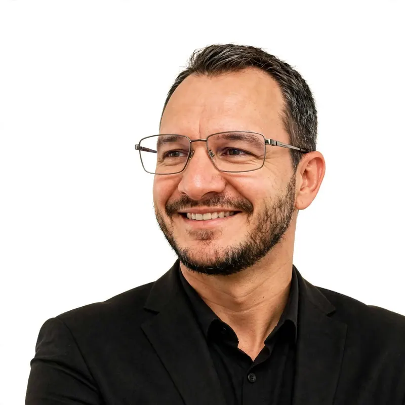 Edilson Paris de óculos e roupa escura, sorrindo, em retrato sobre fundo branco